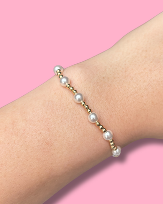 Pearl bracelet on a wrist with a pink background