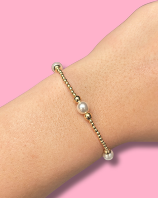 Bracelet with pearls and gold beads on a wrist against a pink background