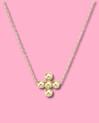 Gold necklace with three round pendants on a pink background