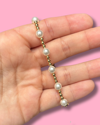 Hand holding a pearl bracelet with gold accents against a pink background