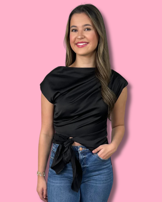 Woman wearing a black top and blue jeans against a pink background