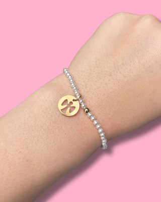 Gold bracelet with a peace symbol and pearl bracelet on a pink background