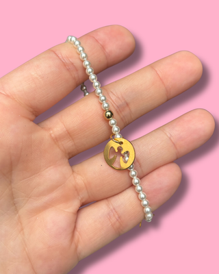 Hand holding a pearl bracelet with a gold charm against a pink background