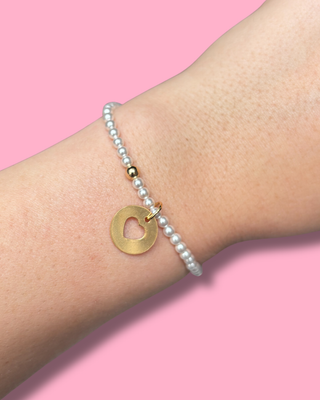 Pearl bracelet with a gold heart pendant on a pink background