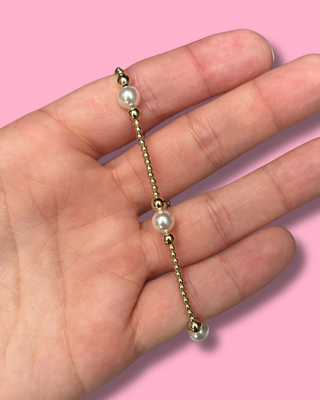 Gold chain with pearls held in a hand against a pink background