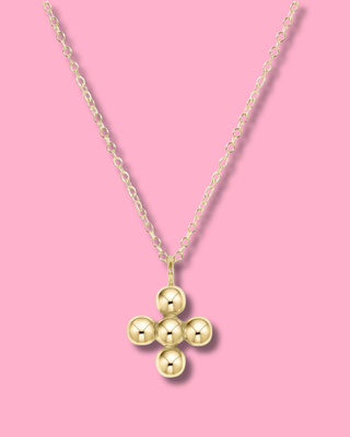 Gold necklace with a three-ball pendant on a pink background