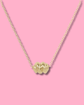 Gold necklace with a heart-shaped pendant on a pink background