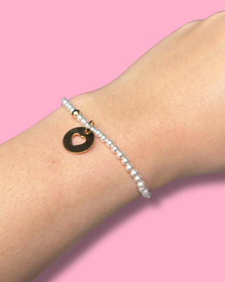 Pearl bracelet with a gold heart pendant on a pink background