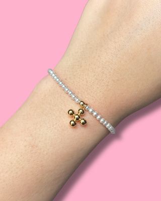 Pearl bracelet with gold beads on a wrist against a pink background