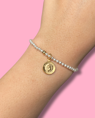 Pearl bracelet with a gold coin charm on a wrist against a pink background