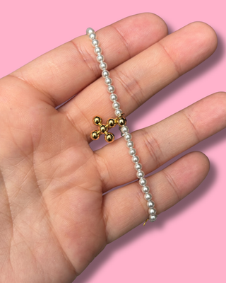 Gold charm on a silver beaded bracelet held in a hand against a pink background