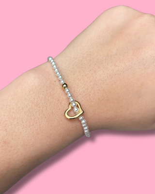 Pearl bracelet with a gold heart charm on a wrist against a pink background