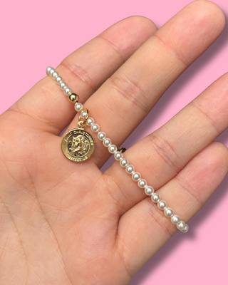 Pearl bracelet with a gold charm held in a hand against a pink background