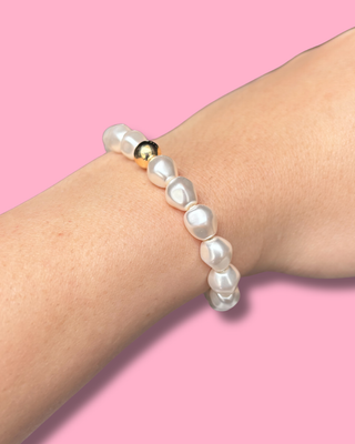 Pearl bracelet on a wrist with a pink background