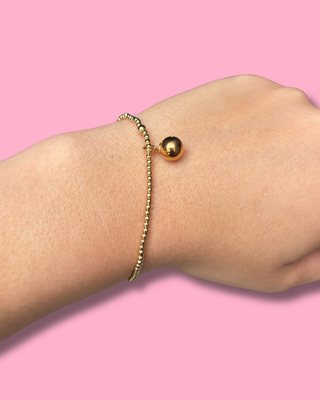 Gold bracelet on a wrist against a pink background