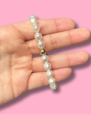 Pearl bracelet with a gold bead on a hand against a pink background
