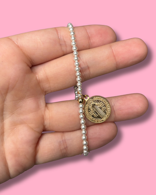 Pearl bracelet with a gold medal held in a hand against a pink background