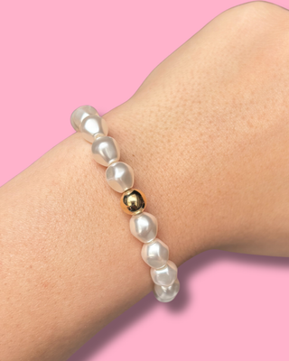 Pearl bracelet with a gold bead on a wrist against a pink background