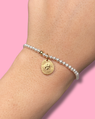 Pearl bracelet with a gold charm on a wrist against a pink background