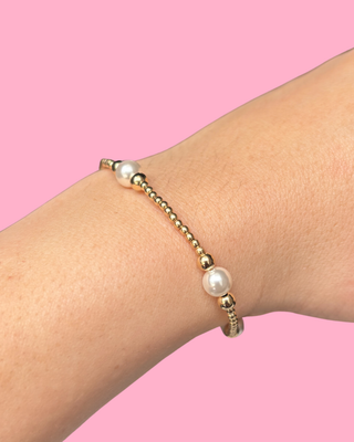 Gold bracelet with pearls on a wrist against a pink background