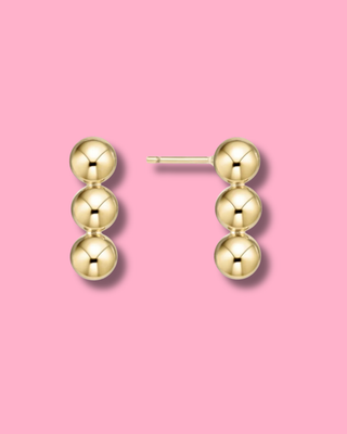 Gold earrings on a pink background