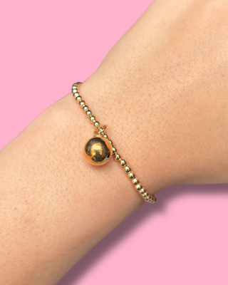 Gold beaded bracelet on a wrist with a pink background