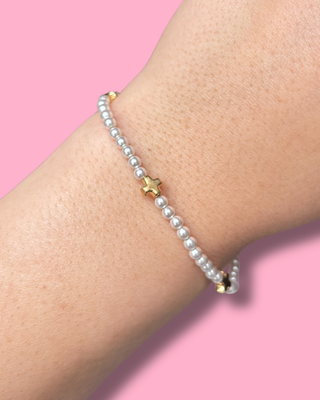 Pearl bracelet with gold accents on a wrist against a pink background