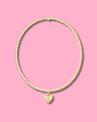 Gold necklace with a heart-shaped pendant on a pink background