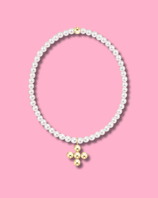 White pearl beaded bracelet with a small gold bead accent at the top and a dangling gold cross charm, displayed on a solid pink background.