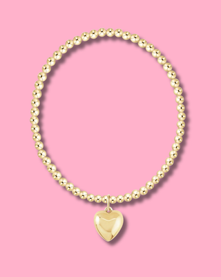 Gold beaded bracelet with a heart-shaped pendant on a pink background