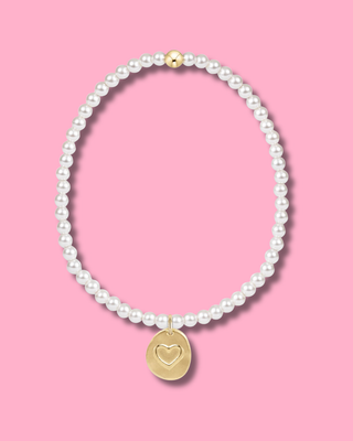 Pearl necklace with a gold heart pendant on a pink background