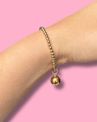 Gold beaded bracelet on a wrist against a pink background