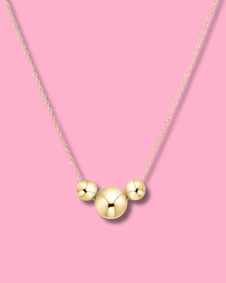 Gold necklace with three round pendants on a pink background