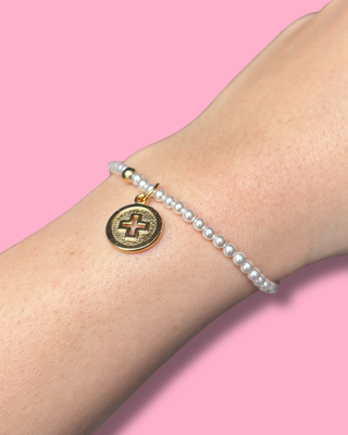 Pearl bracelet with a gold charm on a wrist against a pink background