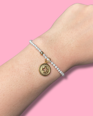 Bracelet with a gold charm on a wrist against a pink background