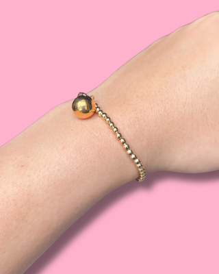 Bracelet with a gold bead on a wrist against a pink background