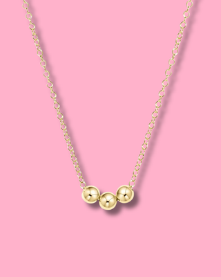 Gold necklace with three round pendants on a pink background