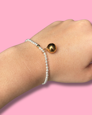 Pearl bracelet with a gold bead on a wrist against a pink background