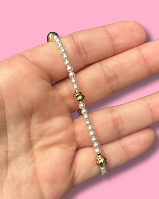 Pearl bracelet with gold accents held in a hand against a pink background