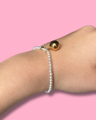 Pearl bracelet and gold beaded anklet on a person's ankle against a pink background