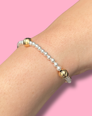 Pearl bracelet with gold beads on a wrist against a pink background