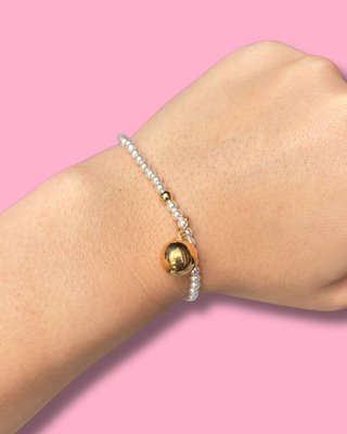 Bracelet with gold heart charm on wrist against pink background