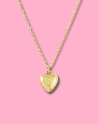 Gold heart-shaped pendant necklace on a pink background