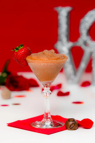 Cocktail in a martini glass with a strawberry garnish on a red background