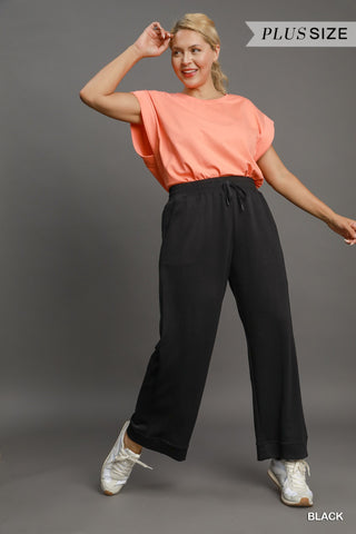 Woman wearing a peach top and black pants on a gray background