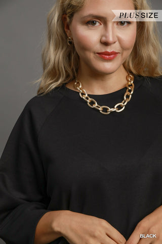 Woman wearing a black top and gold chain necklace with 'Plus Size' text above.