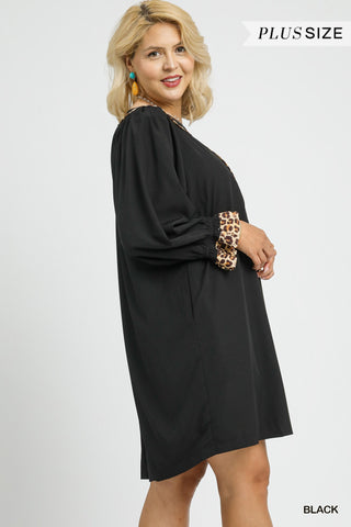 Woman wearing a black dress with leopard print sleeves on a white background