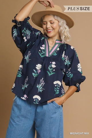 Woman wearing a floral blouse and wide-brimmed hat against a beige background