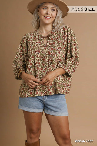 Woman wearing a floral blouse and denim shorts against a beige background