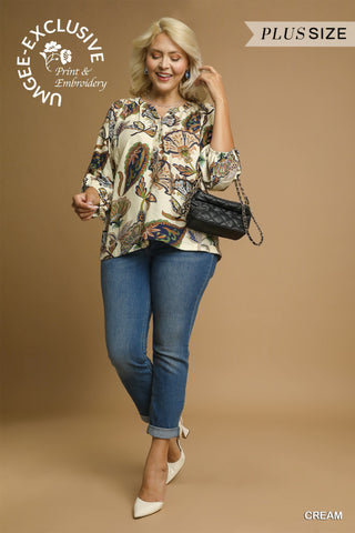 Woman wearing a patterned blouse and blue jeans, holding a black handbag on a beige background.